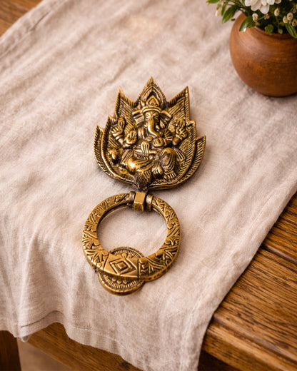 Decorative brass door knocker on a white cloth with a wooden surface and plant in the background