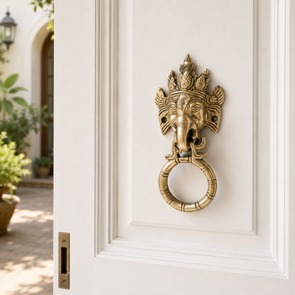 Decorative brass door knocker shaped like a elephant head on a white door.