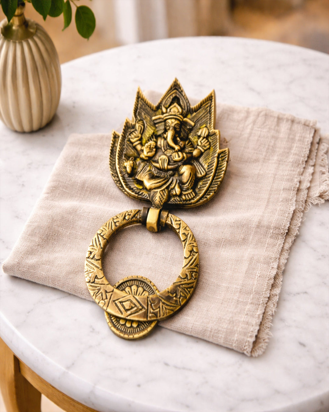 Decorative brass wall hanging on a marble surface with a plant in the background