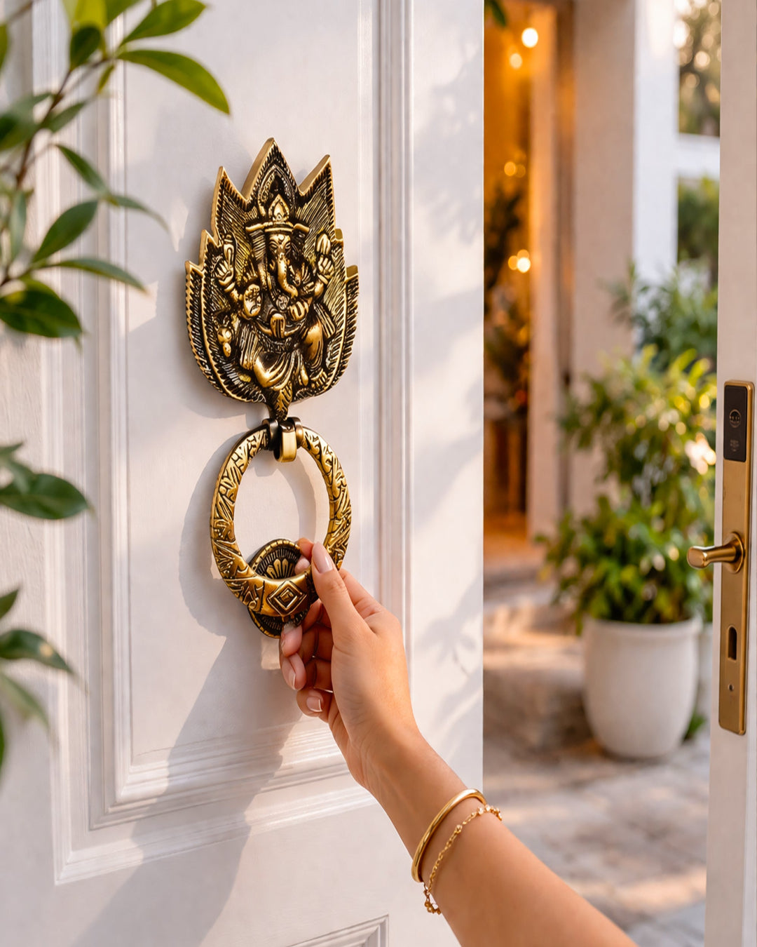 Decorative door knocker on a white door with a hand reaching out to open it, surrounded by plants.