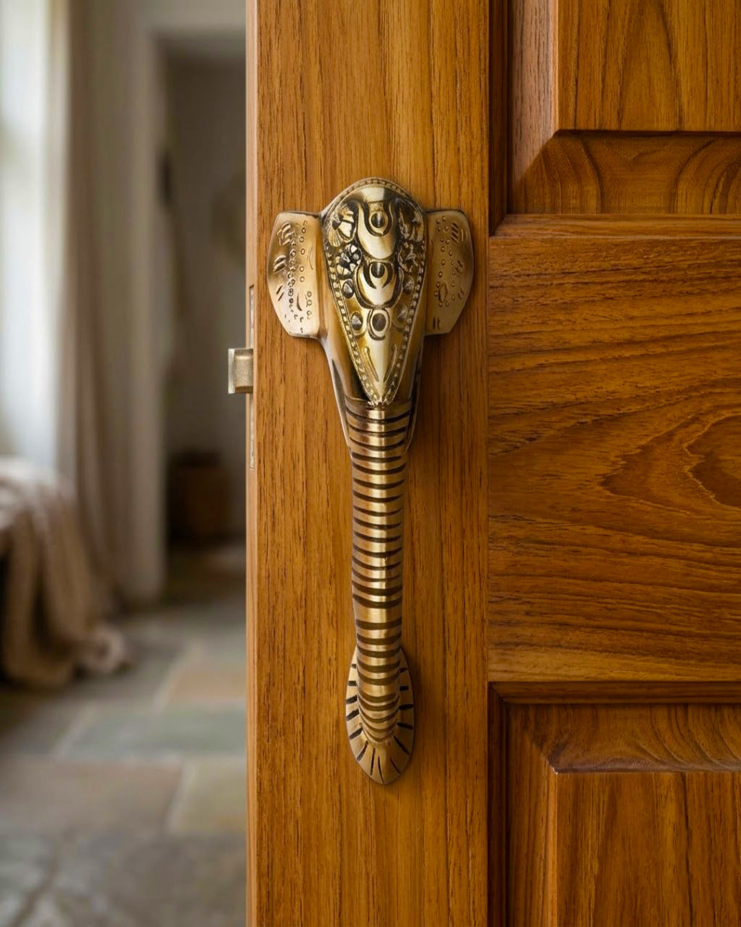 Decorative brass door handle shaped like an elephant on a wooden door.