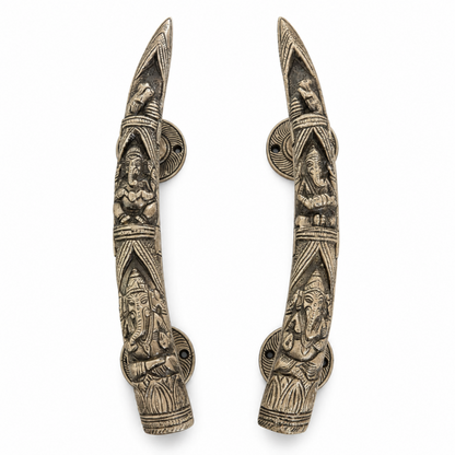 A pair of ornate silver-toned metal door handles featuring detailed carvings of Hindu deities, set against a plain white background.