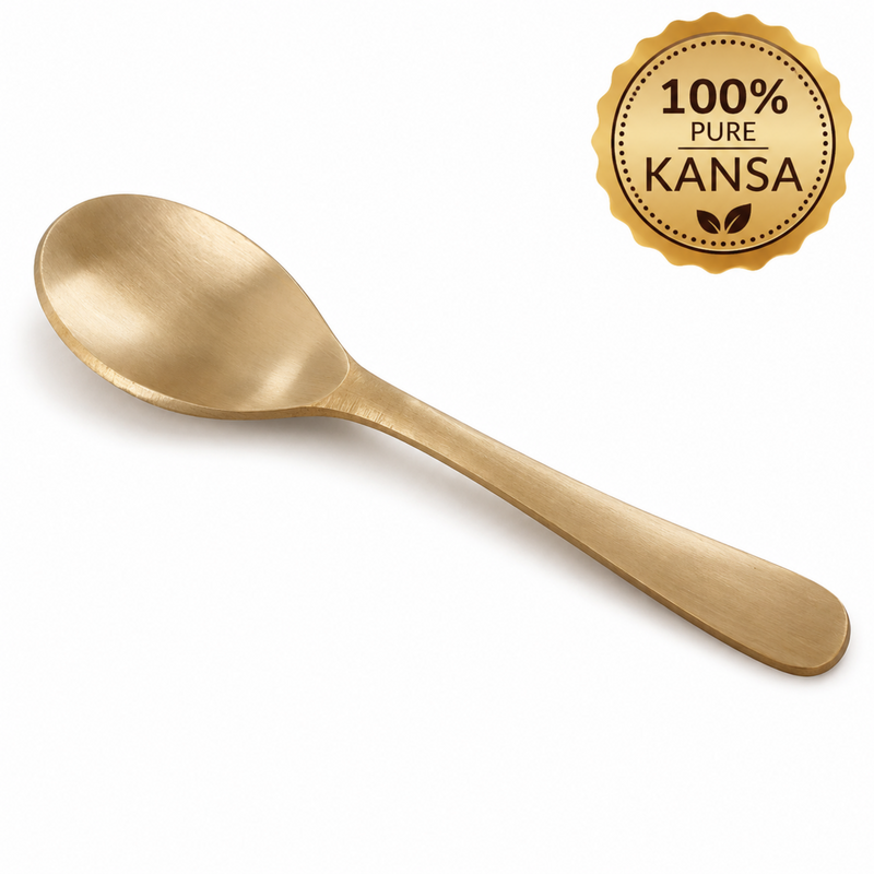 A single gold-colored metal spoon with a brushed finish, shown diagonally on a white background with a gold '100% Pure Kansa' badge in the top right corner.